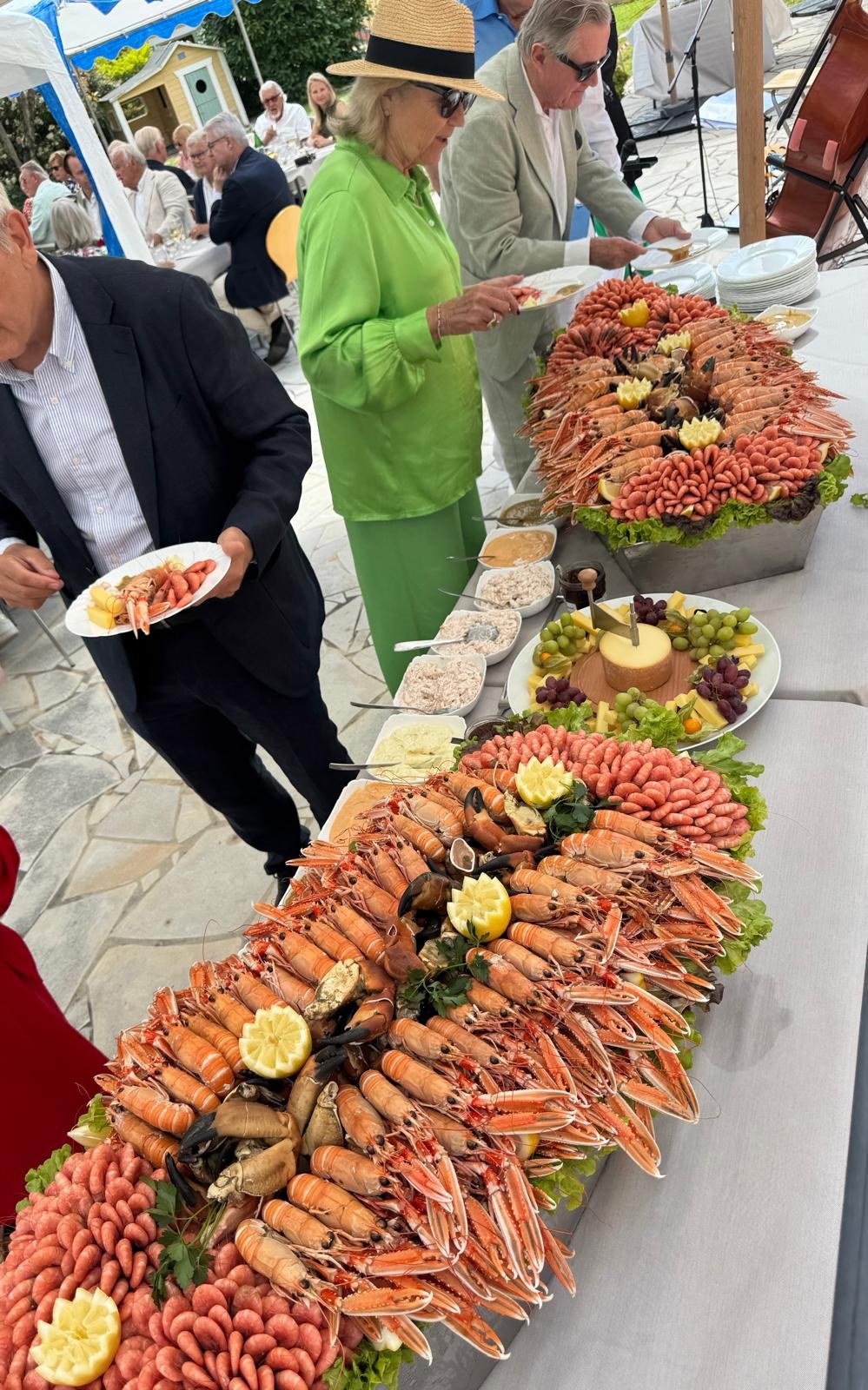 Des invités se servent en langoustines, crevettes et pinces de crabe à un long buffet en plein air